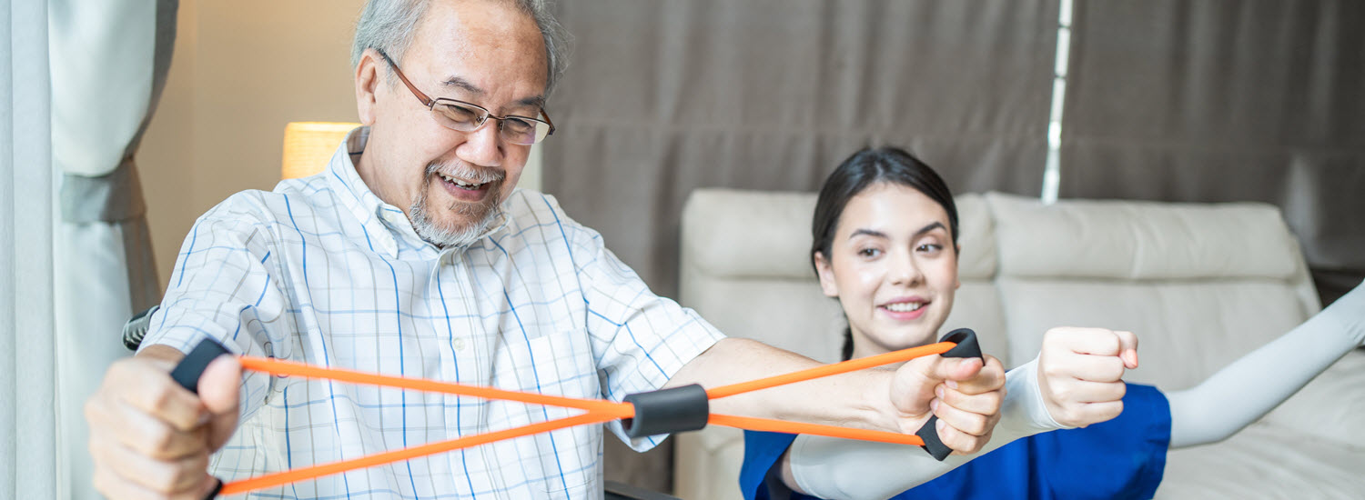 smiling Asian man in a wheelchair works with therapist using stretch bands